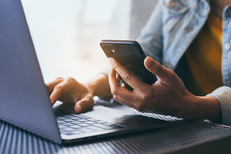 person looking at phone with computer in front of them while sitting at desk