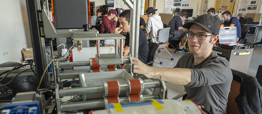 student working with large piece of equipment in lab with other students in background