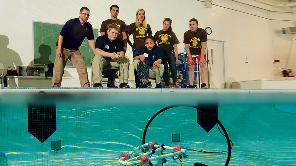 Group of students at indoor pool controlling underwater robot
