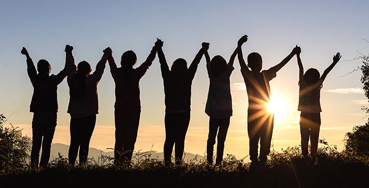 group of people holding hands together up in air with sunset in background
