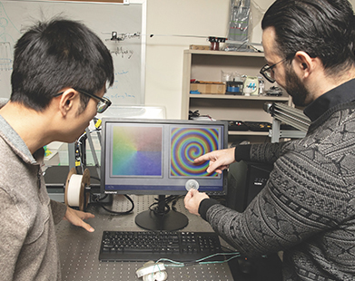 Ph.D. student Chadi Ellouzi (right) shows Chen Shen a 3D printed acoustic lens that can spin sound waves. Their research has shown acoustic waves can propel a miniature robotic swimmer through water.